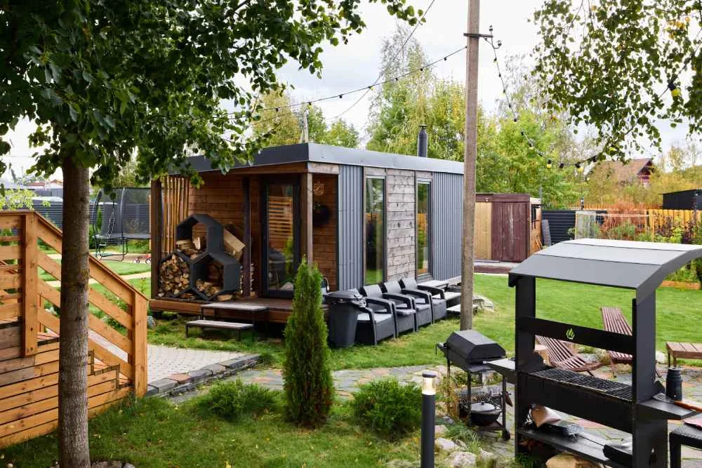 Moderne Gartensauna aus Holz mit Sitzgelegenheiten und Grill im Grünen.